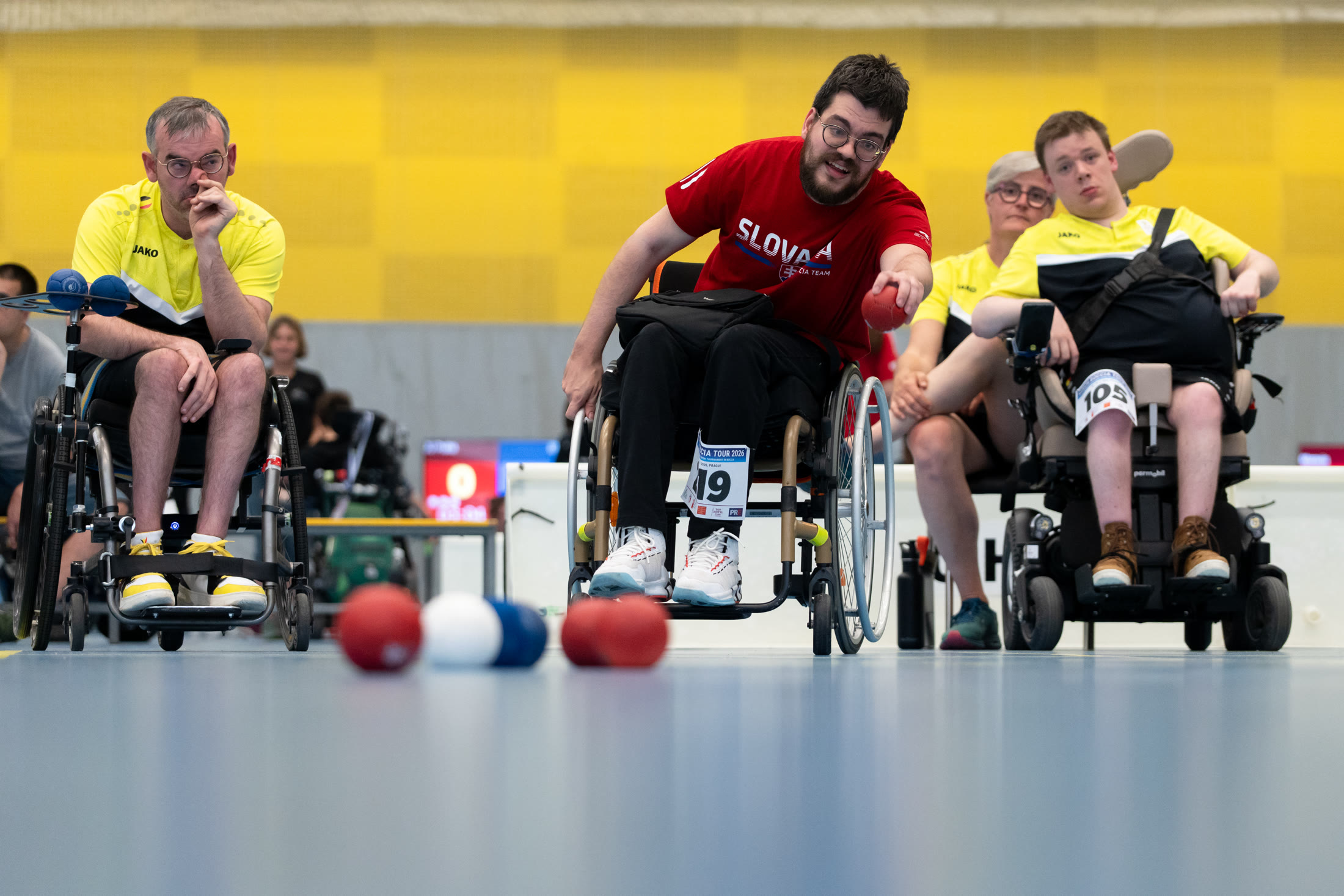 Hráč v boccia turnaji hází míč, diváci sledují hru